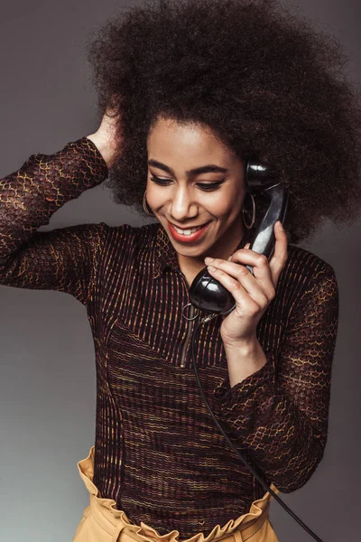 Усміхнена афроамериканська дівчина в стилі ретро розмовляє старовинним стаціонарним телефоном ізольовано на сірому — стокове фото
