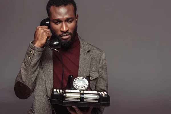 Africano americano retro estilo hombre hablando por vintage estacionario teléfono aislado en gris - foto de stock