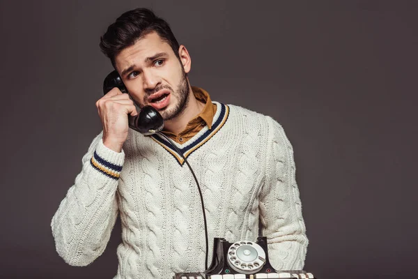 Irritierter, im Retro-Stil gestylter gutaussehender Mann spricht mit einem alten stationären Telefon isoliert auf grau — Stockfoto