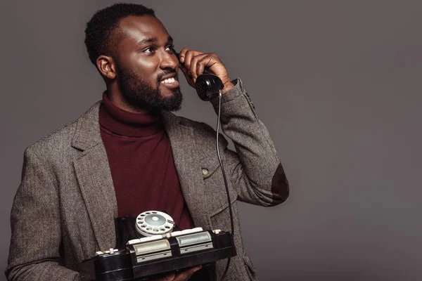 Glücklich afrikanisch-amerikanisch im Retro-Stil Mann spricht mit Vintage-Telefon stationär isoliert auf grau — Stockfoto