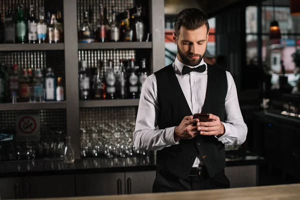 Красивый бармен с помощью смартфона на барной стойке — стоковое фото