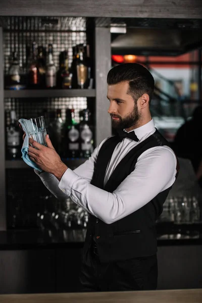Vista lateral de belo bartender limpeza de vidro com pano à noite — Fotografia de Stock