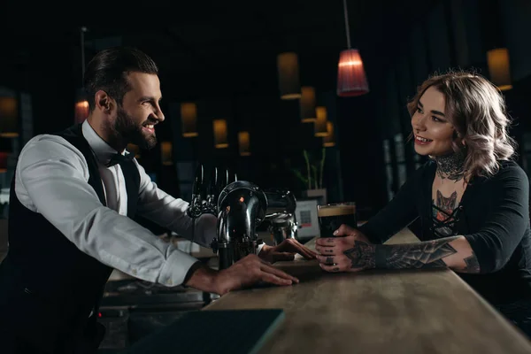 Vista lateral de sorrir barman masculino e menina olhando uns para os outros no balcão de bar — Fotografia de Stock