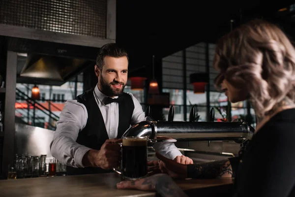 Garçom bonito sorrindo dando copo de cerveja para visitante feminino — Fotografia de Stock