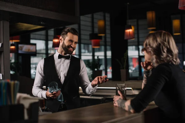 Souriant barman nettoyage verre et parler avec visiteur féminin — Photo de stock