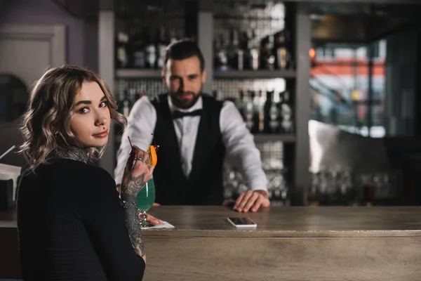 Garçom e garota tatuada olhando para a câmera no balcão de bar — Fotografia de Stock