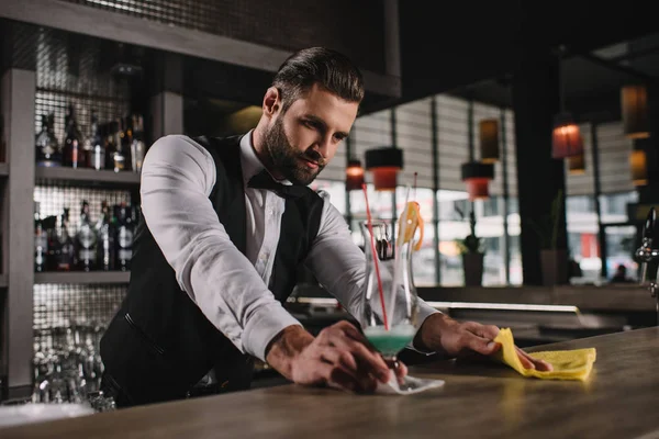 Handsome bartender cleaning bar counter with rag — Stock Photo