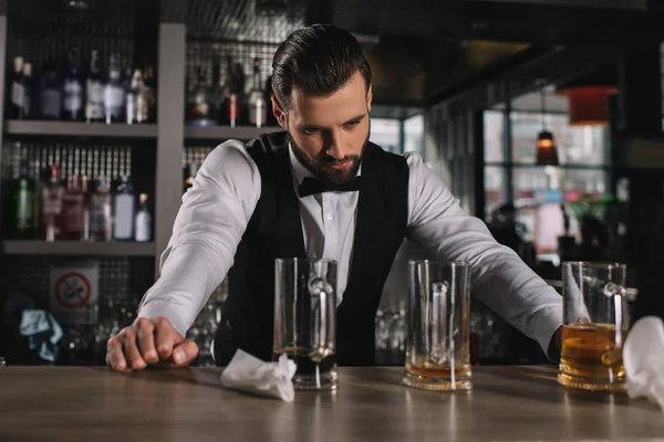 Müder gutaussehender Barkeeper lehnt an der Theke und blickt auf schmutzige Gläser und Müll — Stockfoto