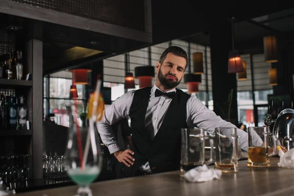 Fatigué barman penché sur le comptoir du bar et regardant des lunettes sales et des ordures — Photo de stock