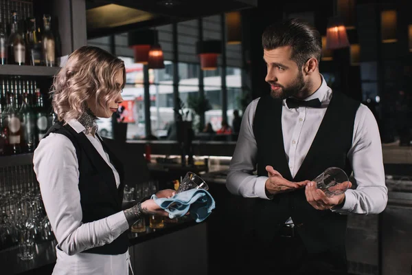 Bartender showing at glass to colleague in bar — Stock Photo