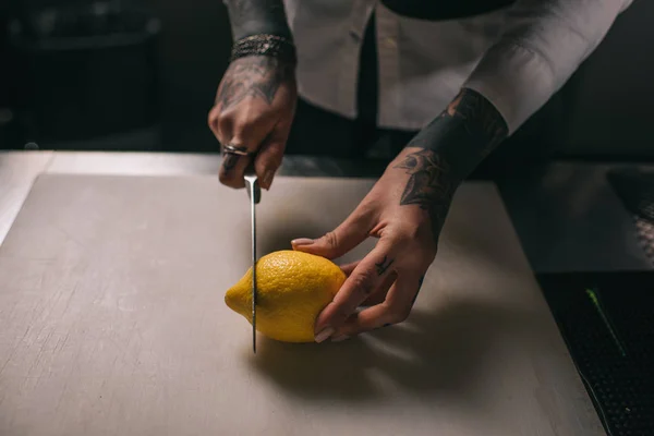 Cropped image of tattooed girl cutting lemon for drinks — Stock Photo