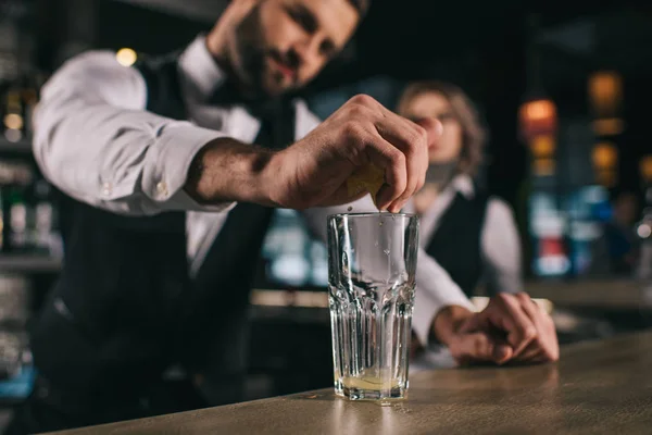 Camarero macho exprimiendo el jugo de limón en un vaso en el bar - foto de stock