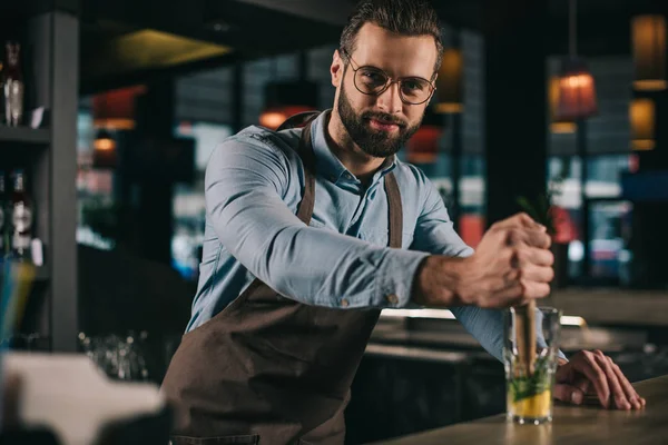 Schöner Barkeeper bereitet Alkoholgetränk zu und schaut in die Kamera — Stockfoto