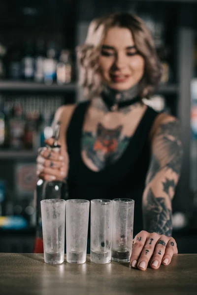Tattooed bartender looking at glasses for shot drinks — Stock Photo
