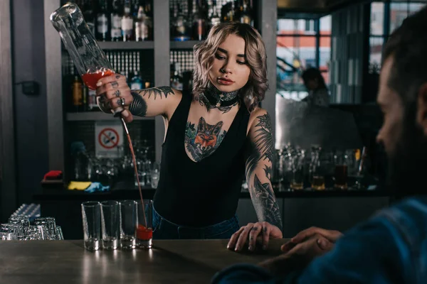 Tattooed bartender making shot drinks for man at bar — Stock Photo