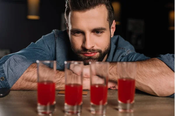 Handsome visitor sitting at bar counter and looking at four shot drinks — Stock Photo