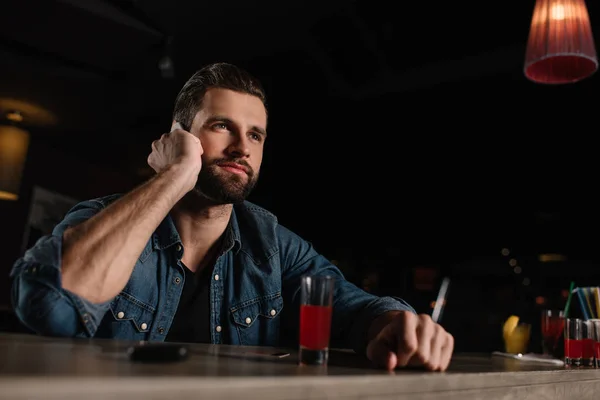 Visitante sentado en el mostrador de bar y hablando por teléfono inteligente - foto de stock