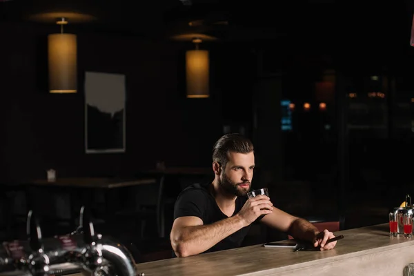 Hombre guapo sentado en el mostrador del bar y beber whisky - foto de stock