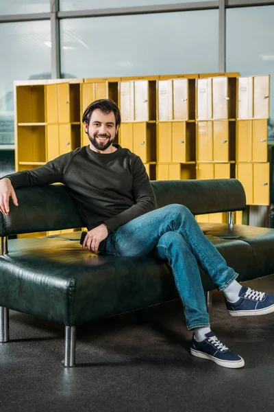 Smiling man looking at camera while resting on sofa in skate park — Stock Photo