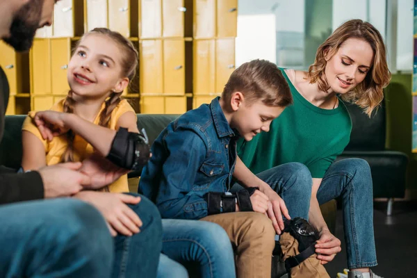 Partial view of parents helping kids to wear protection before skating in skate park — Stock Photo