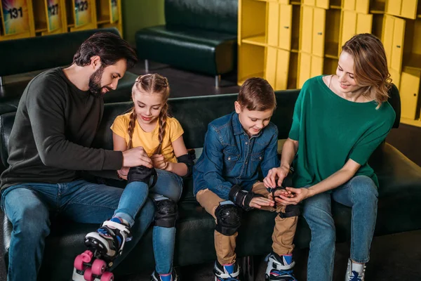 Padres ayudando a los niños a usar protección antes de patinar en skate park - foto de stock