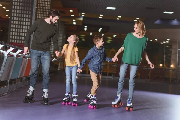 Família feliz de mãos dadas enquanto patinam juntos na pista de patins — Fotografia de Stock