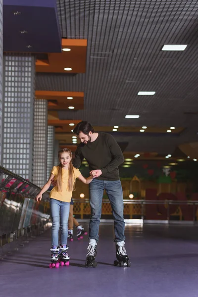 Father and daughter holding hands while skating together on roller rink — Stock Photo