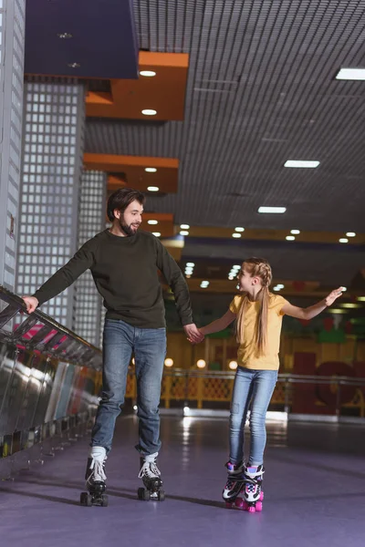 Father and daughter holding hands while skating together on roller rink — Stock Photo