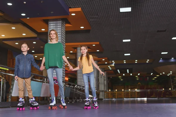Mother and kids holding hands while skating together on roller rink — Stock Photo