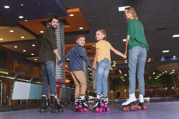 Vista trasera de la familia tomados de la mano mientras patinan juntos en la pista de patinaje - foto de stock