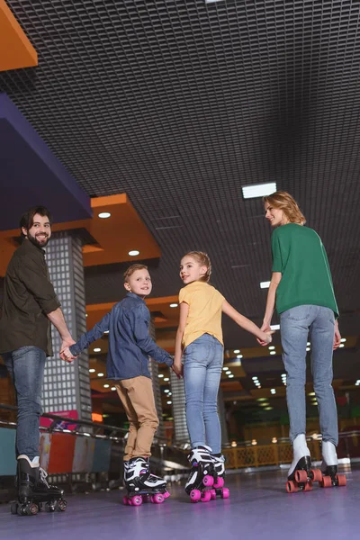 Vista trasera de la familia tomados de la mano mientras patinan juntos en la pista de patinaje - foto de stock