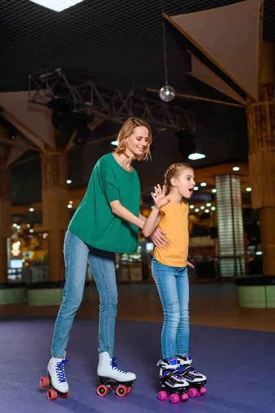 Smiling mother and little daughter skating together on roller rink — Stock Photo