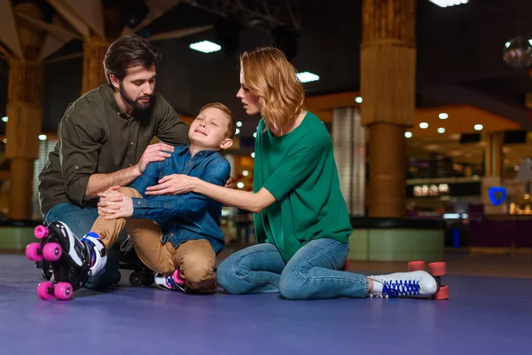 Родители успокаивают плачущего сына на роликовых коньках на катке — стоковое фото