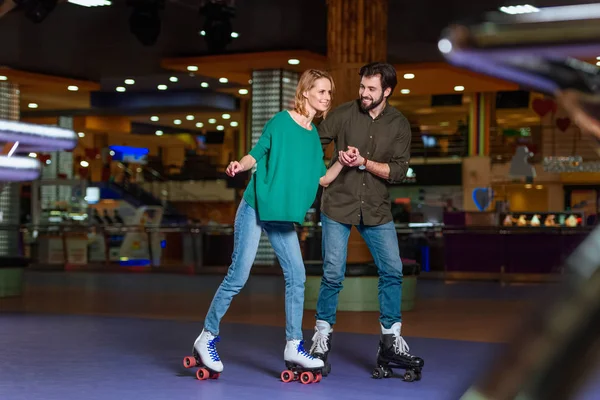 Young couple holding hands while skating together on roller rink — Stock Photo