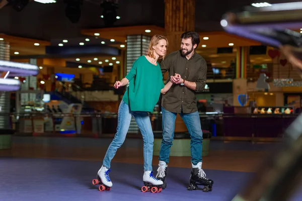 Jovem casal de mãos dadas enquanto patinavam juntos na pista de patins — Fotografia de Stock