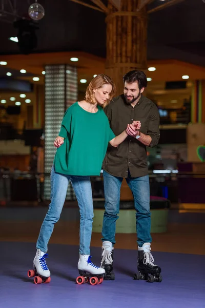 Young couple holding hands while skating together on roller rink — Stock Photo
