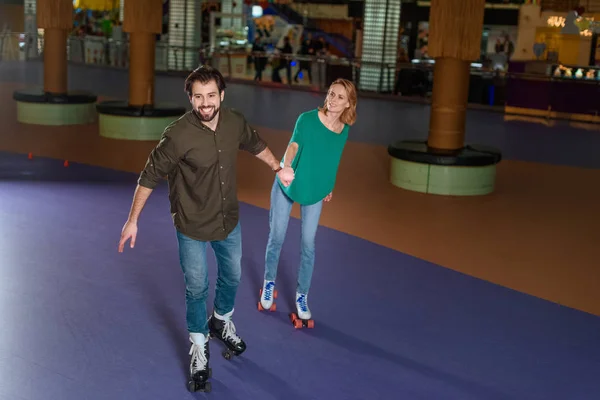 Jovem casal de mãos dadas enquanto patinavam juntos na pista de patins — Fotografia de Stock