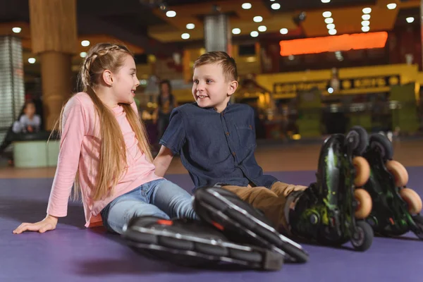 Mignons frères et sœurs en patins à roulettes se reposant après avoir patiné sur la patinoire à roulettes — Photo de stock