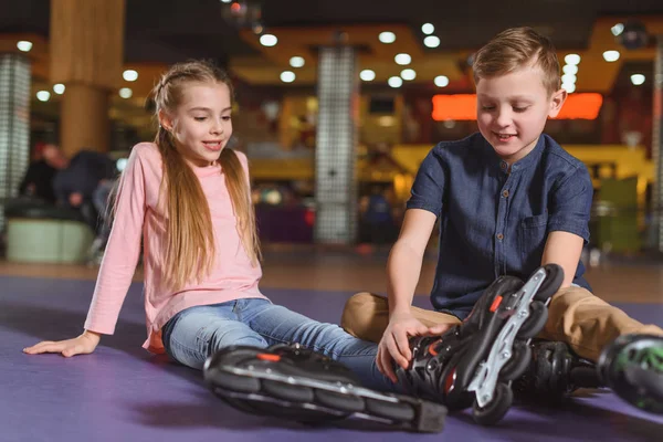 Mignons frères et sœurs en patins à roulettes se reposant après avoir patiné sur la patinoire à roulettes — Photo de stock