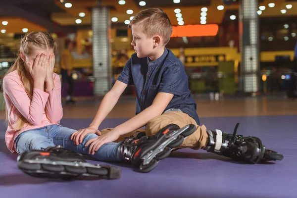 Brother cheering up crying sister in roller skates on roller rink — Stock Photo