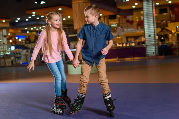 Adorable kids holding hands while skating together on roller rink — Stock Photo