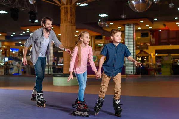 Отец и маленькие дети катаются вместе на роликовых коньках — стоковое фото