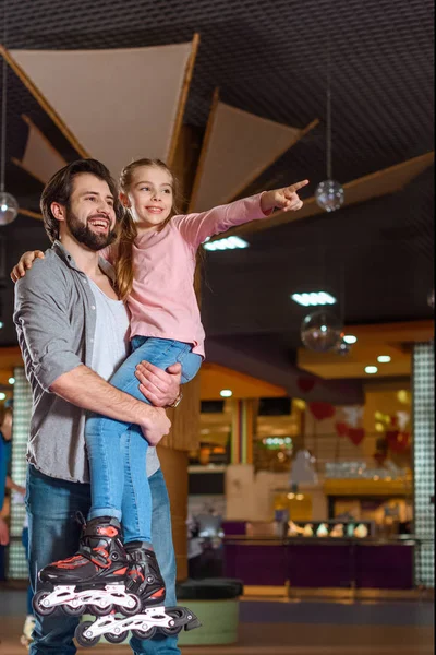 Padre sorridente che tiene figlia in pattini a rotelle sulla pista di pattinaggio — Foto stock