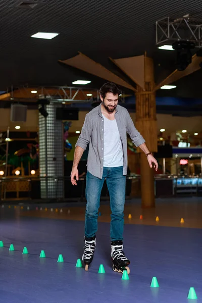 Uomo sorridente in pattini a rotelle pattinaggio su pista di pattinaggio con coni — Foto stock