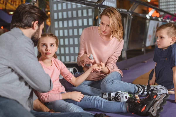 Enfoque selectivo de la madre desinfectando a las pequeñas hijas lesionadas mano en pista de patinaje - foto de stock