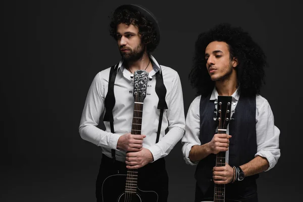 Duet of handsome young musicians with acoustic guitars looking away on black — Stock Photo