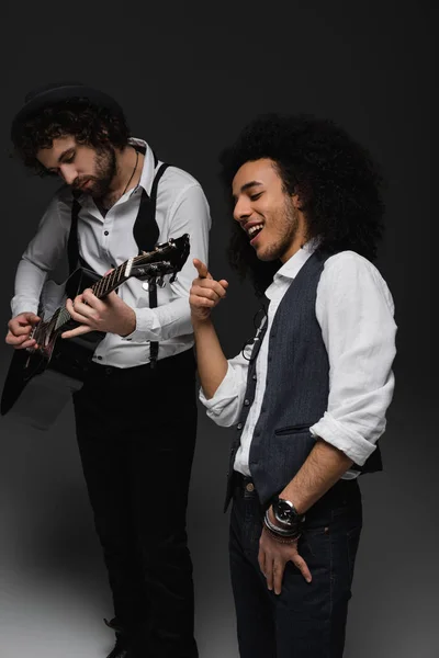 Joven dúo de músicos tocando la guitarra y cantando en negro - foto de stock