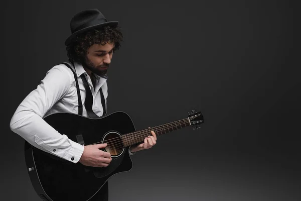 Beau musicien barbu jouant de la guitare acoustique sur noir — Photo de stock