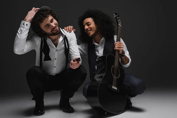 Duetto di musicisti felici con chitarra e armonica seduta accovacciata — Foto stock