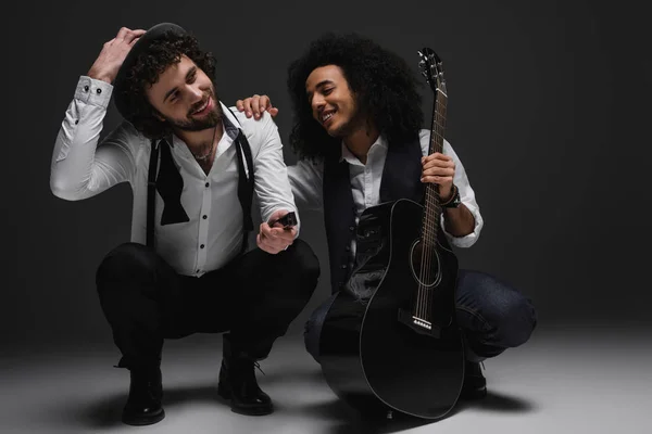 Duet of happy musicians with guitar and harmonica sitting squat — Stock Photo